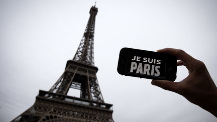 Une personne brandit un téléphone avec le slogan "Je suis Paris" devant la tour Eiffel, le 14 novembre 2015, au lendemain des attentats. (JOEL SAGET / AFP)