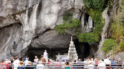 Des fidèles assistent à une messe devant la grotte de Massabielle, à Lourdes, le 16 juillet 2021. (LUDOVIC MARIN / AFP)