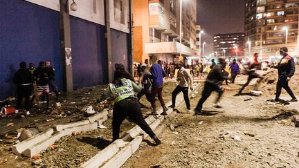 Des manifestants s'enfuient après que des policiers ont ouvert le feu&nbsp;avec des balles en caoutchouc dans le quartier de Jeppestown, à Johannesburg, le 11 juillet 2021. Plusieurs magasins y ont été pillés et des voitures incendiées. (LUCA SOLA / AFP)