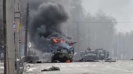 Un&nbsp;véhicule blindé russe brûle à côté du corps d'un soldat non identifié lors d'un combat avec les forces armées ukrainiennes, à Kharkiv (Ukraine), le 27 février 2022. (SERGEY BOBOK / AFP)