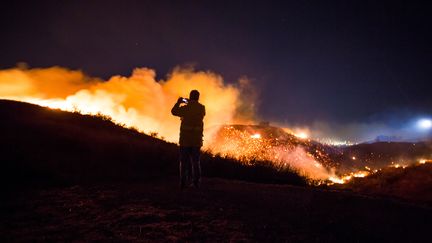 Un homme prend en photo le spectaculaire incendie "Creek", le long d'une colline proche du quartier de Shadow Hills à Los Angeles, le 5 décembre 2017. (KYLE GRILLOT / AFP)