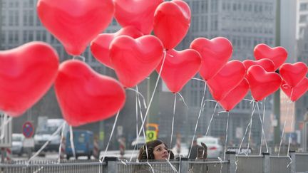 Une jeune femme accroche un ballon en forme de coeur sur une grille &agrave; Berlin (Allemagne), le 14 f&eacute;vrier 2012. (STEPHANIE PILICK / DPA)