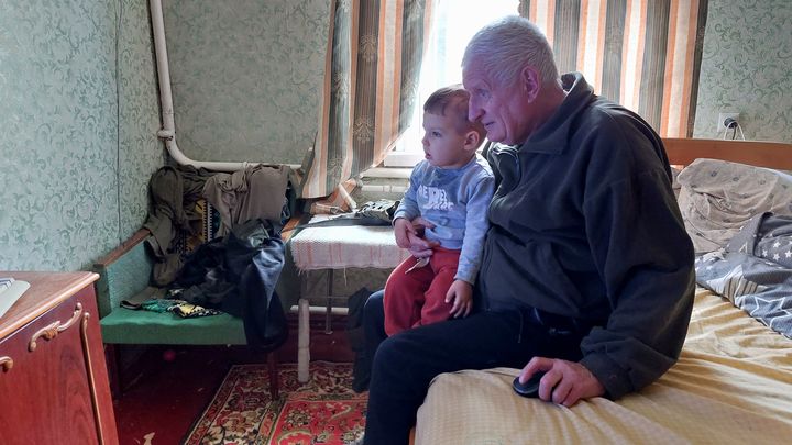 Mark sur les genoux de son grand-père Anatoli, en train d'écouter du folklore ukrainien. (AGATHE MAHUET / FRANCEINFO / RADIO FRANCE)