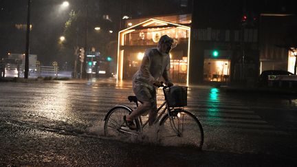 Un cycliste tente de faire fasse à la pluie et au vent dans les rues de Tokyo (Japon), le 9 septembre 2019. (CHARLY TRIBALLEAU / AFP)