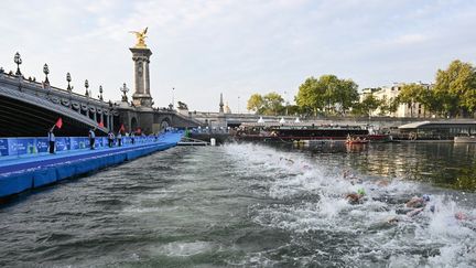 Les triathlètes nagent dans la Seine près du pont Alexandre III lors de l'épreuve test des Jeux Olympiques mondiaux de triathlon masculin 2023 à Paris, le 18 août 2023. (BERTRAND GUAY / AFP)