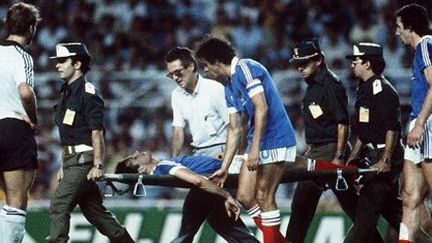 Le défenseur français Patrick Battiston est emmené sur une civière après un choc violent avec le gardien allemand Harald Schumacher le 8 juillet 1982 lors de la demi-finale de Coupe du monde de football à Séville. Il est réconforté par le capitaine de l'équipe de France, Michel Platini. (AFP )