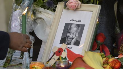 Une femme place une bougie pr&egrave;s d'un portrait de Nelson Mandela, sur la place Parliament square &agrave; Londres (Royaume-Uni), le 6 d&eacute;cembre 2013. (TOBY MELVILLE / REUTERS)