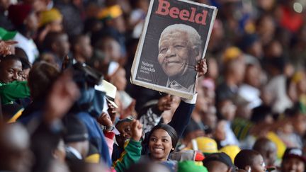 Une femme brandit un portrait de l'ancien président sud-africain Nelson Mandela lors de la cérémonie d'hommage à son honneur organisée le&nbsp;10 décembre 2013 au Soccer City Stadium de Johannesburg. L'icône de la lutte anti-apartheid est morte cinq jours plus tôt à l'âge de 95 ans. (ROBERTO SCHMIDT / AFP)