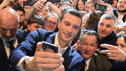 Jordan Bardellan se prend en photo avec des personnes venues l'écouter en meeting à Montbéliard, le 22 mars 2024. (PATRICK HERTZOG / AFP)