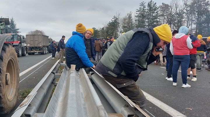 Des agriculteurs assis près d'une glissière de sécurité démontée, le 23 janvier 2024, sur l'échangeur n°7 de l'A62, au niveau de la commune du Passage (Lot-et-Garonne). (FABIEN MAGNENOU / FRANCEINFO)