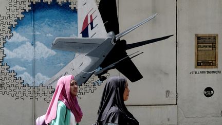 Des habitantes de la ville de Shah Alam (Malaisie) passent devant une fresque représentant le Boeing 777 de la Malaysia Airlines disparu, mardi 8 mars 2016. (MANAN VATSYAYANA / AFP)