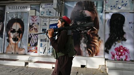 Un taliban devant un salon de beauté dont les visages de femmes en vitrine ont été occultés, à Kaboul (Afghanistan), le 18 août 2021. (WAKIL KOHSAR / AFP)