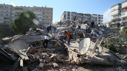 Des personnes recherchent des rescapés dans un&nbsp;immeuble effondré à Izmir, en Turquie, le 30 octobre 2020. (MEHMET EMIN MENGUARSLAN / ANADOLU AGENCY / AFP)