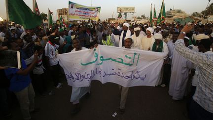 Des membres de la communauté soufie soudanaise se joignent le 20 mai 2019 au sit-in devant le siège de l'armée à Khartoum, brandissant un calicot sur lequel on peut lire : "Le soufisme, uni comme les doigts d'une main contre les commerçants de la religion et les terroristes". (ASHRAF SHAZLY / AFP)