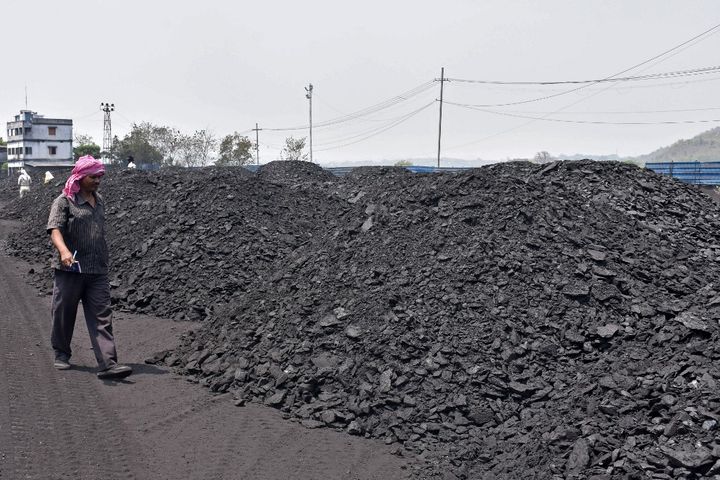 A worker walks past piles of coal at the Amrapali coal mines in Peeparwar, in the Indian state of Jharkhand, on April 30, 2022. (- / AFP)