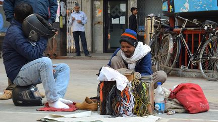  
Mochin Bablu a 45 ans. Sa cordonnerie tient dans une boîte en bois qu’il installe à même le sol. Il répare, cire, vend des lacets depuis 35 ans. Son salaire mensuel avoisine lui aussi les 50 euros par mois.  (Amanda Jacquel)