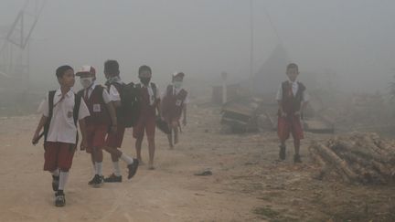 Des enfants sur le chemin de l'école passent, le 14 octobre 2019, à Palembang (Indonésie) dans des feux de forêts dont les fumées provoquent des émissions à effet de serre et aggravent le réchauffement climatique. (ABDUL QODIR / AFP)