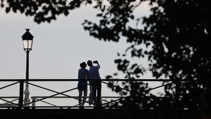 Un couple se prend en photo sur le pont des Arts à Paris le 12 juillet 2022. (LUDOVIC MARIN / AFP)