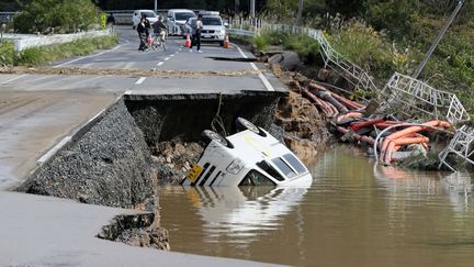 Un véhicule est renversé dans un ravin formé par l'effondrement d'une route lors du typhon Hagibis, le 14 octobre 2019, à Mito City (Japon). (KOICHI NALAMURA / YOMIURI / AFP)