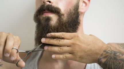 Un homme tatou&eacute; se coupe la barbe avec une paire de ciseaux. (HERO IMAGES / GETTY)