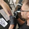 Vassil réalise un tatouage en forme de trident sur le mollet d'un client, Kiev, le 3 juin 2022. (ERIC AUDRA / RADIO FRANCE)