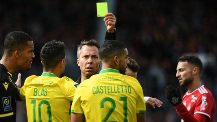 L'arbitre français Johan Hamel&nbsp;(C)&nbsp;montre un carton jaune au défenseur&nbsp;de Nantes Jean-Charles&nbsp;Castelletto&nbsp;lors du match de football français de Ligue 1&nbsp;entre Brest et Nantes au stade Francis Le-Blé de Brest, le 10 avril 2022. (FRED TANNEAU / AFP)