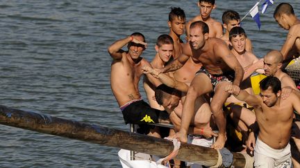 Un homme tente d'attraper un drapeau en marchant sur un poteau cir&eacute; lors de la f&ecirc;te de la "cuca&ntilde;a", sur le fleuve&nbsp;Guadalquivir pr&egrave;s de S&eacute;ville (Espagne), le dimanche 22 juillet 2012. (CRISTINA QUICLER / AFP)