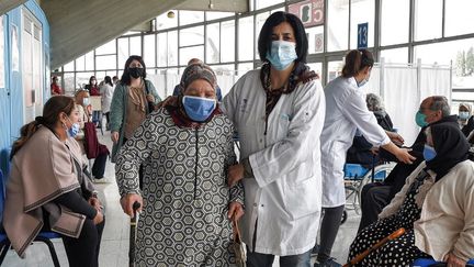 Une&nbsp;infirmière&nbsp;accompagne&nbsp;une femme âgée pour recevoir une dose du vaccin contre le coronavirus à la salle de sport El-Menzah à Tunis, le 12 avril 2021. (FETHI BELAID / AFP)