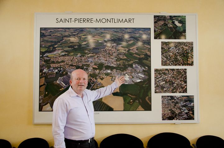 Le maire de Saint-Pierre-Montlimart (Maine-et-Loire), Serge Piou, devant une photo de la ville, le 15 avril 2015. Le bois juste au-dessus de sa main correspond &agrave; la zone inconstructible &agrave; cause des galeries de l'ancienne mine. (THOMAS BAIETTO / FRANCETV INFO)