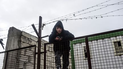 Sur une barrière, le 6 février 2016, un garçon est le spectateur de l'attente des Syriens qui fuient le nord de la ville d'Alep à Bab-Al Salam, près d'Azaz, ville située à la frontière avec la Turquie. Les forces gouvernementales syriennes appuyées par les frappes aériennes russes sont à l'origine de cet exode. L'offensive de grande ampleur lancée par Damas et ses alliés dans la région d'Alep, la deuxième ville du pays qui pourrait être bientôt totalement encerclée, a torpillé le démarrage des pourparlers de paix à Genève sous l'égide des Nations unies. Le chef de la diplomatie syrienne Walid Moualem a déclaré samedi 6 février 2016 qu'il n'y aurait pas de cessez-le-feu tant que la Jordanie et la Turquie maintiendraient leurs frontières ouvertes. La manoeuvre d'encerclement lancée par les forces de Bachar al-Assad vise à isoler les quartiers rebelles d'Alep où vivaient encore récemment quelque 350.000 personnes, contre environ un million dans la partie gouvernementale de la ville. (BULENT KILIC / AFP)