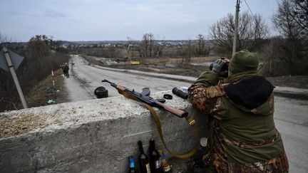 Un militaire ukrainien regarde à travers des jumelles vers la ville de Stoyanka à un poste de contrôle avant le dernier pont sur la route qui relie Stoyanka à Kiev, le 6 mars 2022. (ARIS MESSINIS / AFP)