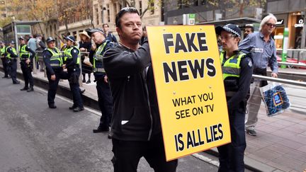 Un manifestant en Australie brandit une pancarte où est inscrit "Fake news, ce que vous voyez à la télévision n'est que mensonge" (WILLIAM WEST / AFP)