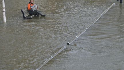 Une femme lit le journal assise sur un banc inond&eacute; par la Tamise &agrave; Staines (Royaume-Uni), le 17 f&eacute;vrier 2014. (TOBY MELVILLE / REUTERS)