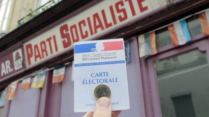 Un sympathisant présente sa carte électorale ainsi qu'une pièce d'un euro devant une permanence du Parti socialiste à Paris en janvier 2011 (JACQUES DEMARTHON / AFP)