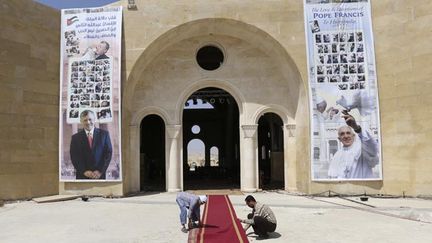 &nbsp; (© REUTERS/Muhammad Hamed - Des travailleurs déroulent un tapis devant une église de Jordanie pour préparer l’arrivée du pape.)