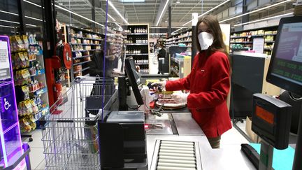 Une caissière équipée d'un masque de protection et derrière une vitre en Plexiglas encaisse les achats d'une cliente à Auch (Gers), le 17 mars 2020. (SEBASTIEN LAPEYRERE / HANS LUCAS / AFP)