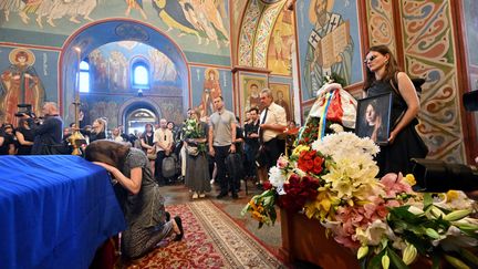 Une femme s'agenouille sur le cercueil de l'écrivaine ukrainienne Victoria Amelina lors d'une cérémonie d'hommage, à Kiev, le 4 juillet 2023. (SERGEI SUPINSKY / AFP)