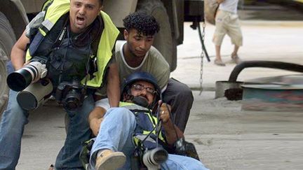 un photographe de Reuters, est blessé à la jambe par un tir apparemment palestinien, durant des affrontements entre soldats israéliens et palestiniens dans la ville de Naplouse en Cisjordanie, le 29 mai 2003.

Il est aidé par un autre photographe, Alaa Badarneh, de l’EPA (European Pressphoto Agency) et un jeune homme non identifié. (AFP PHOTO/JAAFAR ASHTIYEH)