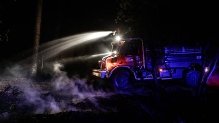 Un fourgon de pompiers progresse au milieu des arbres en arrosant le sol. Les braises sont encore vives au sol. Une progression des flammes visuellement peu impressionnante, mais redoutable. Des hectares de pin&egrave;de continuent de partir en fum&eacute;e. (THIBAUD MORITZ / MAXPPP)