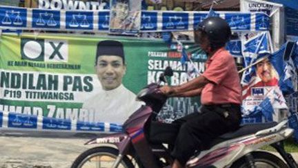 ​Kuala Lumpur, en Malaisie, le 3 mai 2013: un motocycliste passe devant bannières et affiches du Parti national Barisan.  ( AFP PHOTO / ROSLAN RAHMAN )