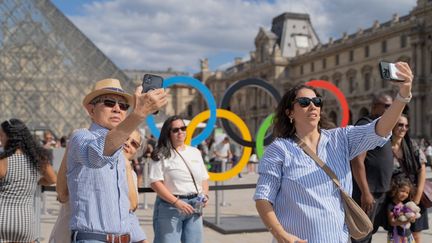 Des touristes se prenant en photo devant les anneaux olympiques au Louvre. (CLAIRE SERIE / HANS LUCAS / AFP)