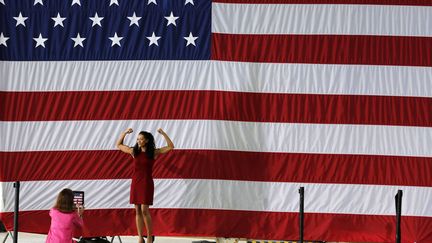 Une jeune femme pose devant le drapeau am&eacute;ricain &agrave; l'issue d'un discours du pr&eacute;sident Barack Obama &agrave; Charlottesville (Virginie), le 29 ao&ucirc;t 2012. (LARRY DOWNING / REUTERS)