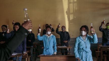 Des élèves brandissent une bouteille de Covid Organics, une tisane présentée par le président malgache Andry Rajoelina comme un puissant remède contre le Covid-19, dans le centre d'Antananarivo, le 23 avril 2020. (RIJASOLO / AFP)