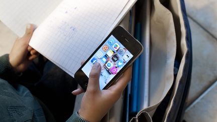 Un élève en train de faire ses devoirs avec un telephone portable a la main. (Photo d'illustration) (SEBASTIEN JARRY / MAXPPP)