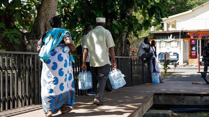 Residents of Mayotte carry packs of water received during a distribution, September 21, 2023. (CHAFION MADI / AFP)