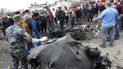 Des forces de sécurité et des passants observent les lieux d'une attaque à la bombe, le 2 janvier 2017, à Bagdad (Irak). (SABAH ARAR / AFP)