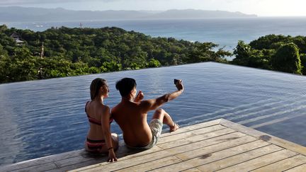 Deux jeunes gens se prennent en photo au bord d'une piscine, aux Philippines, le 7 décembre 2018.&nbsp; (ALEJANDRO ERNESTO / DPA / AFP)