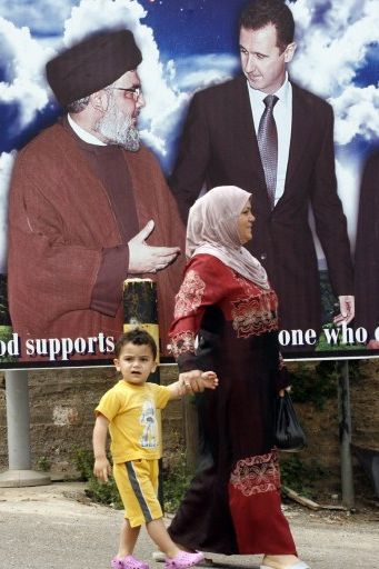 Naqoura, au Liban, le 8 mai 2013: une Libanaise et son enfant passent devant une affiche montrant le chef du Hezbollah Hassan Nasrallah et le président syrien Bachar al-Assad. Il y est inscrit: «Si Dieu vous aide, il n'y a personne qui peut vous vaincre». (AFP PHOTO / MAHMOUD Zayyat)