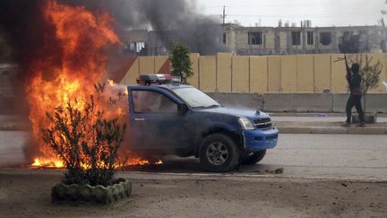 Un combattant d'Al-Qa&iuml;da monte la garde pr&egrave;s d'un v&eacute;hicule de la police incendi&eacute;, &agrave; Fallouja (Irak), le 1er janvier 2014. (AP / SIPA )