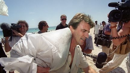 Le ministre français de la Santé et de l'Action humanitaire Bernard Kouchner charge l'un des sacs de riz donnés par des écoliers français, le 05 décembre 1992 sur la plage à côté du port de Mogadiscio. (ERIC FEFERBERG / AFP)